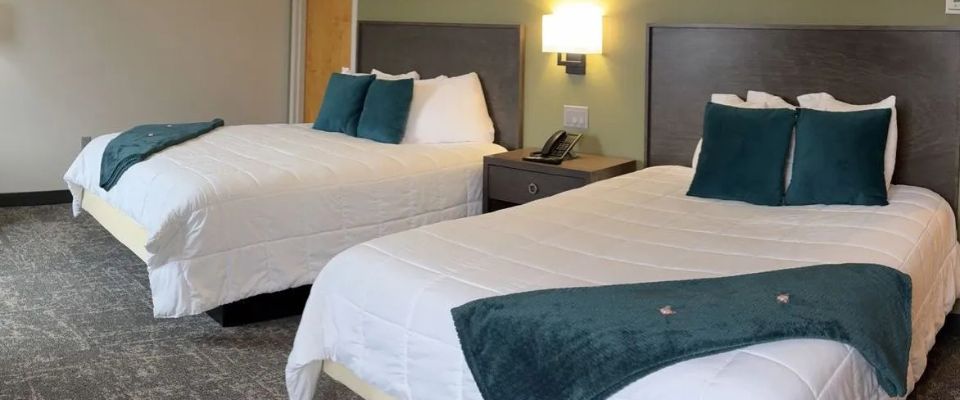 A standard hotel room with two beds, dark headboards, and teal accents.