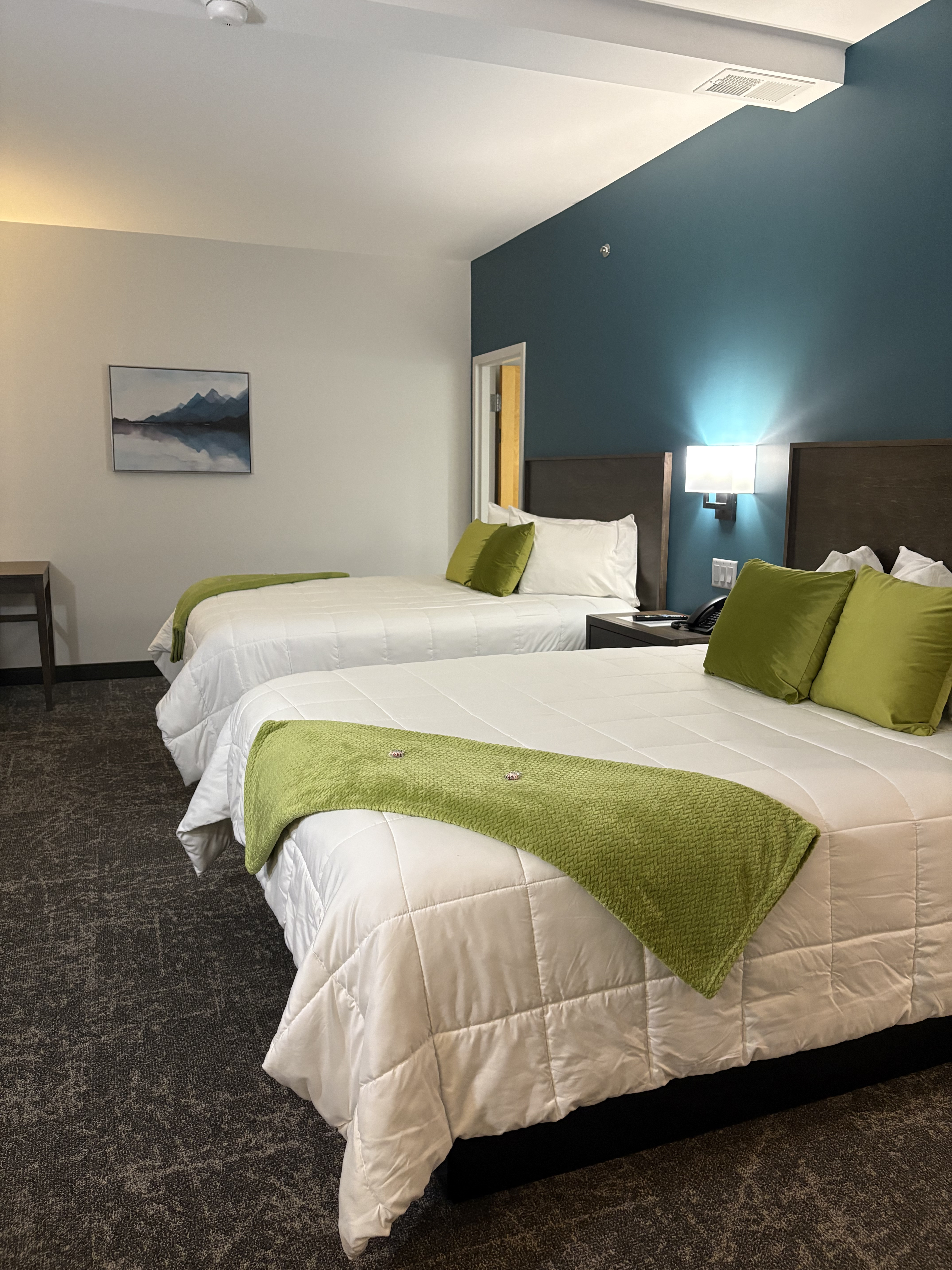 A hotel room with two beds, green accents, and a blue accent wall.