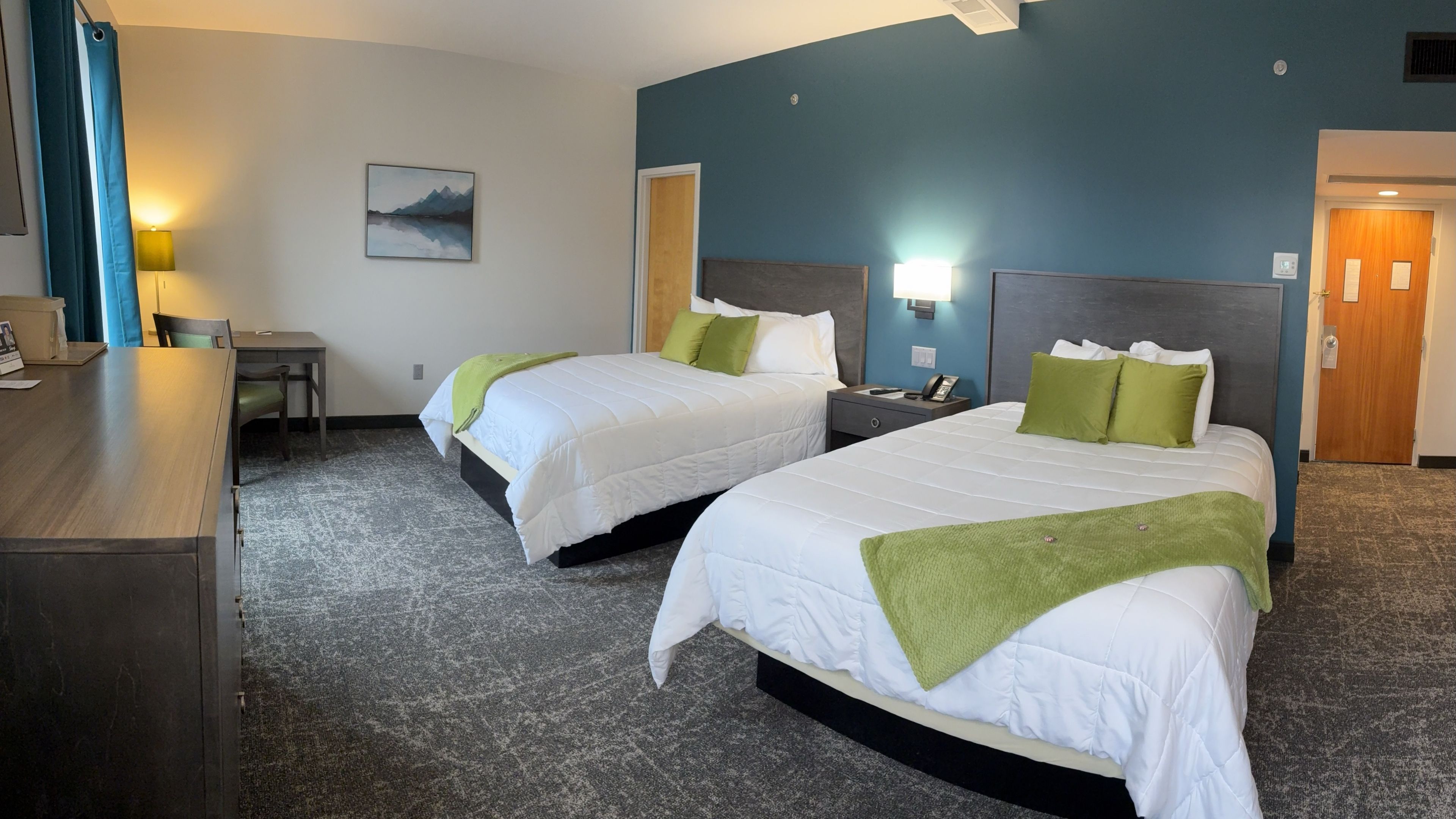 A hotel room with two beds, a desk, and a nightstand.