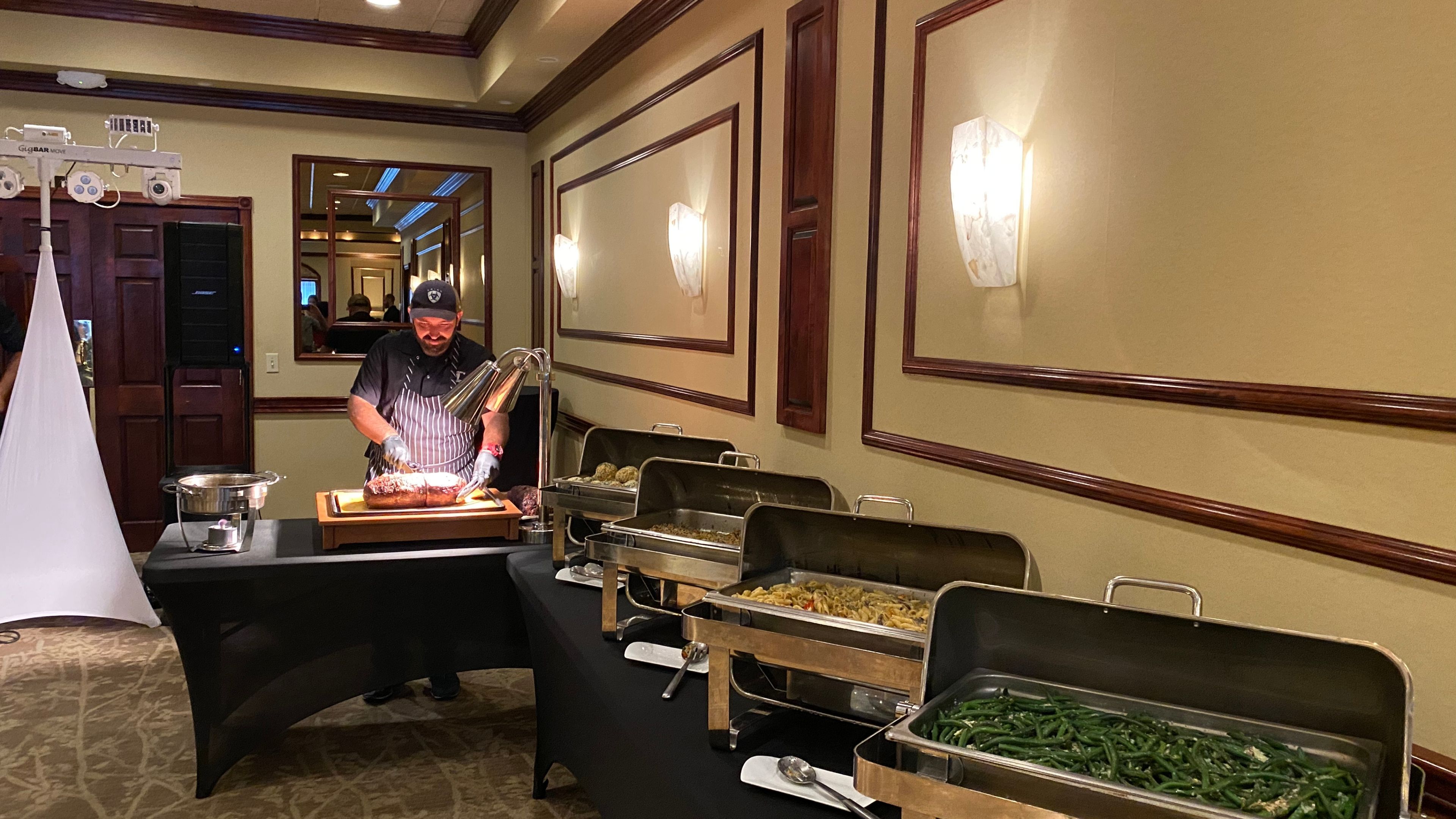 A server stands beside a buffet table with various dishes.
