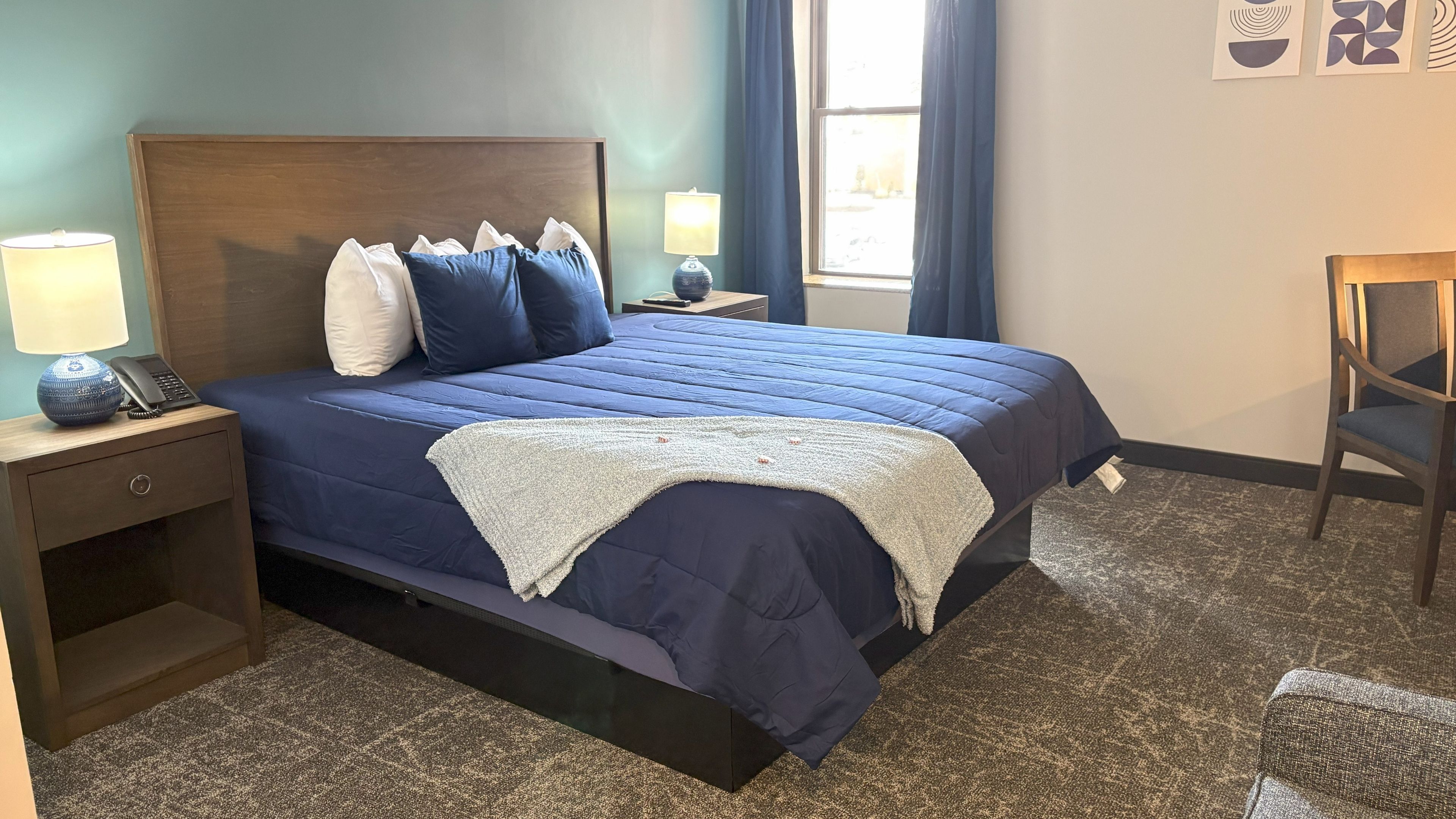 A neatly made hotel room with a blue bedspread, wooden headboard, and modern furnishings.