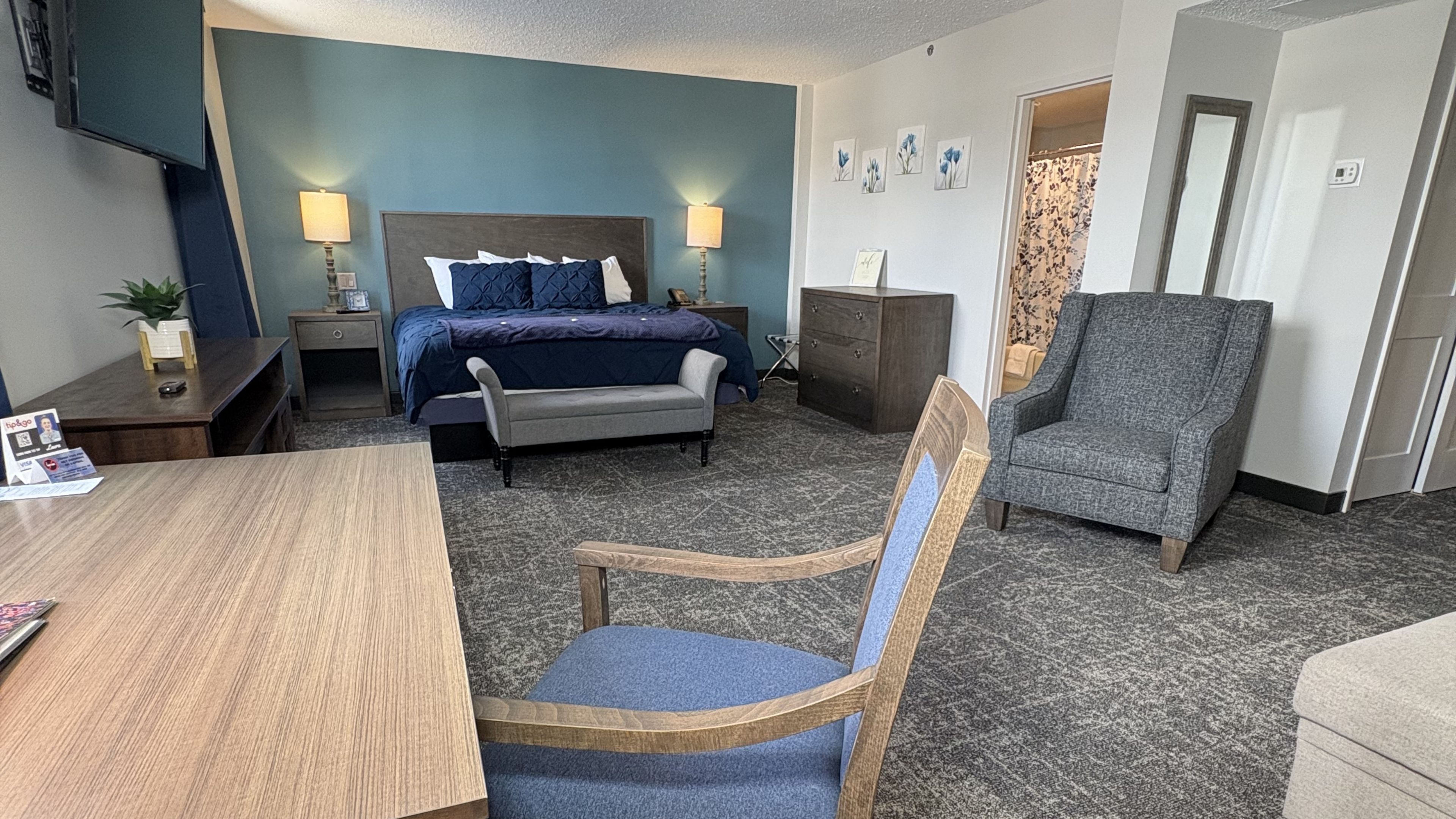 A wide view of a hotel room with a bed, desk, chair, and TV.